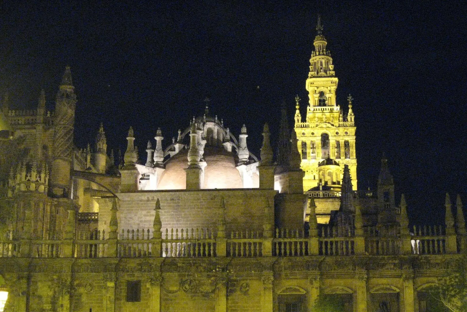 Seville Cathedral and the Giralda tower floodlit in gold against a dark sky