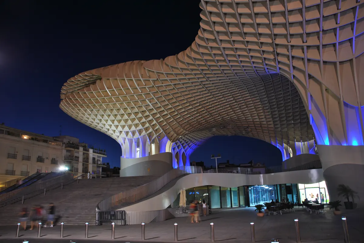 The glazed ground floor of the Metropol Parasol at night, with a broad staircase on the left and the timber lattice curving overhead